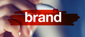 Mão segurando caneta vermelha, sublinhando a palavra 'brand'.